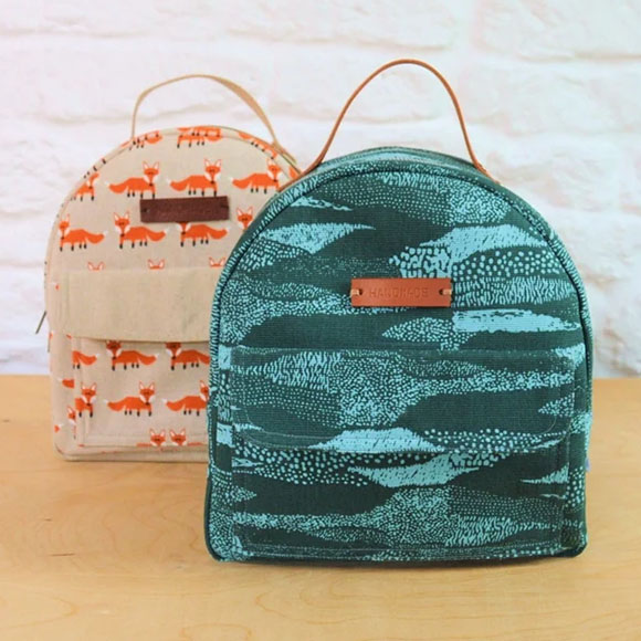 two unisex Mini Backpacks, one with a blue seafoam pattern, and another with a fox pattern