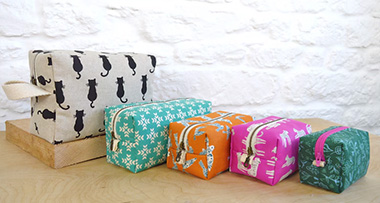 five boxy pouches on a table, four in the small size offered, and one in the larger size