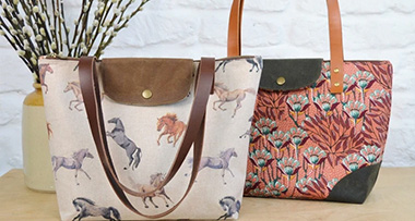 two tote bags sitting on a wooden table with Potpourri sticks in a vase next to them